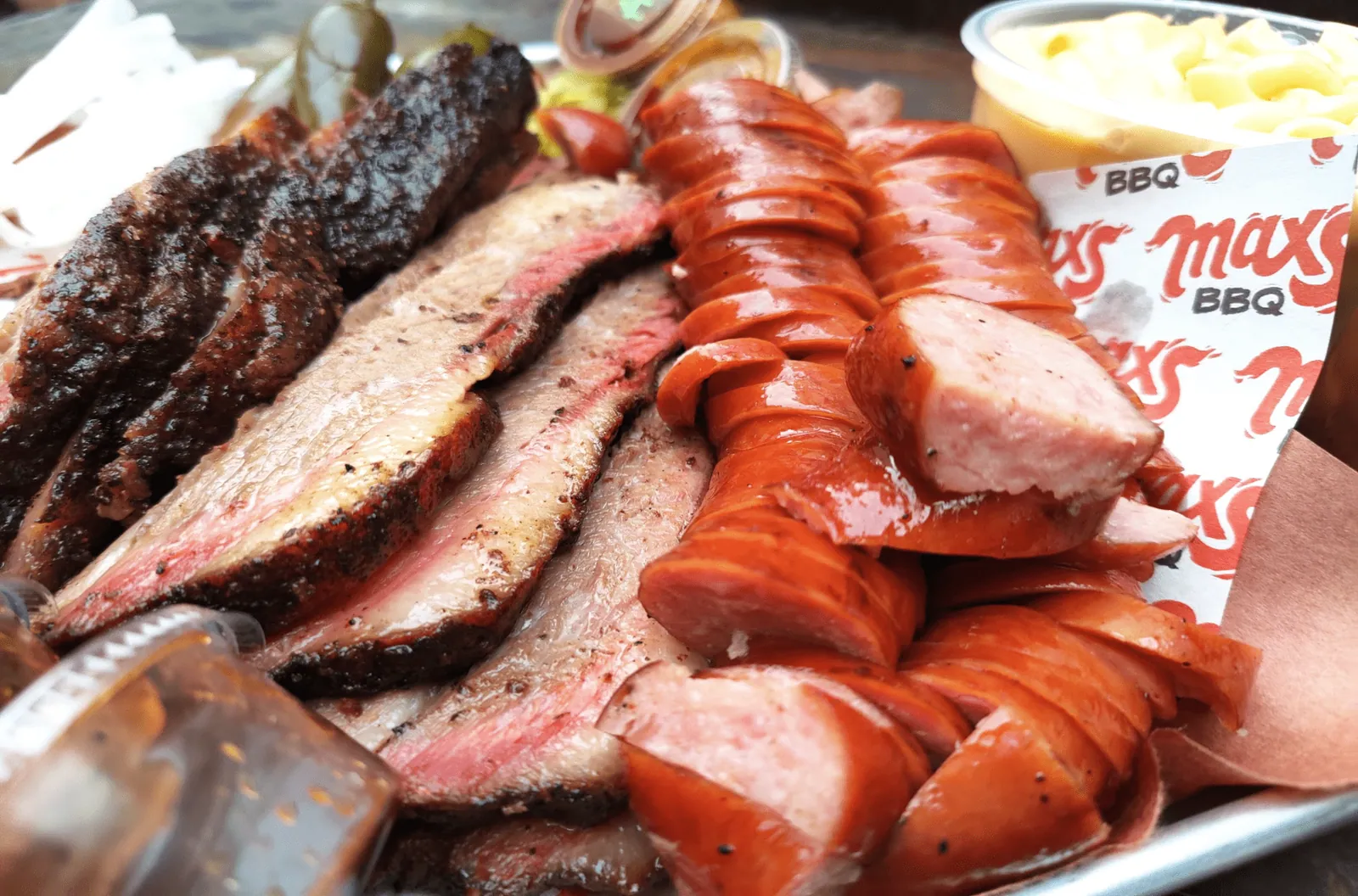 Bandeja con costillar, brisket rebanado, salchicha en rodajas y un vaso de mac n' cheese
