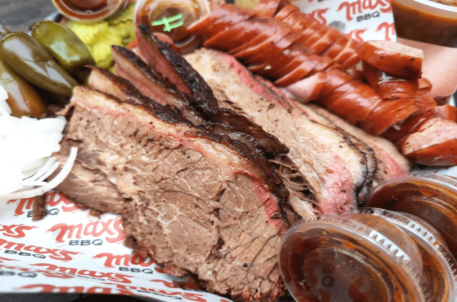 Primer plano de brisket rebanado con su anillo de humo, salchicha en rodajas y salsa BBQ