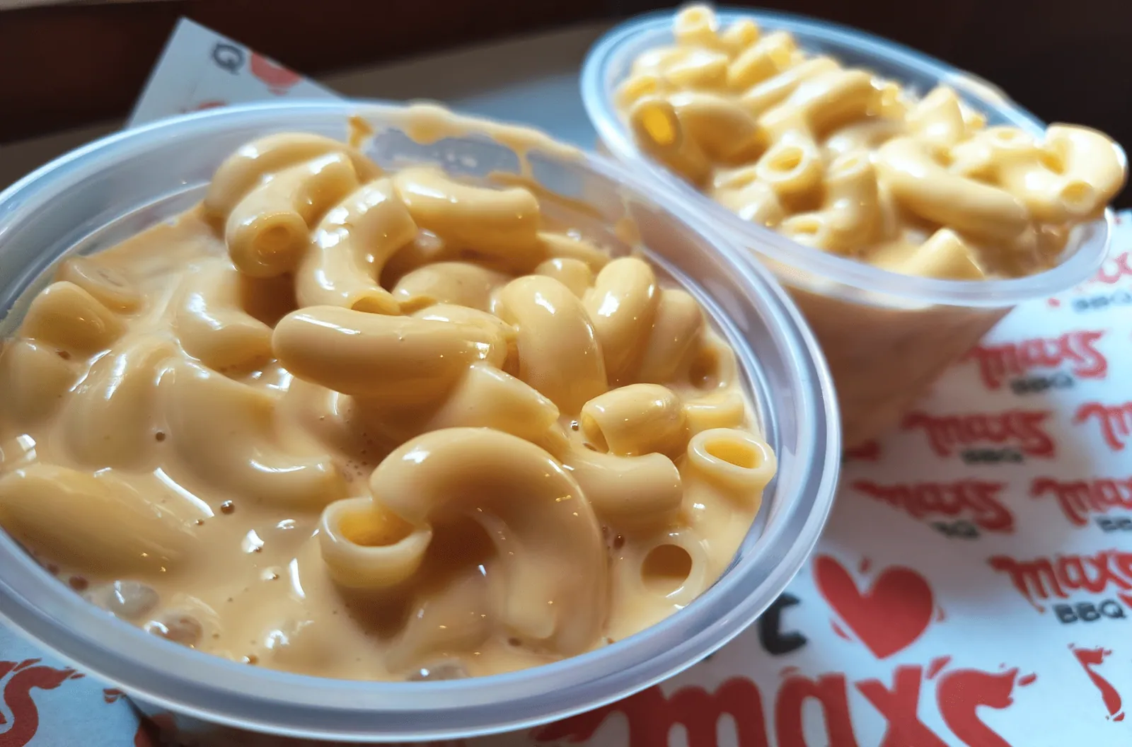 Dos vasos de mac n' cheese para llevar sobre papel de Max's BBQ