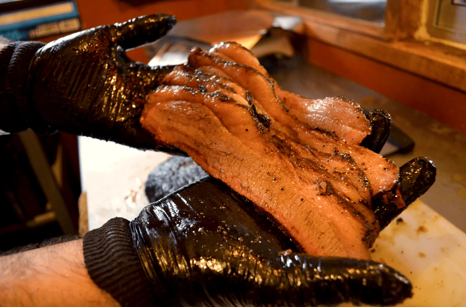 Manos con guantes negros separando las hebras de un brisket ahumado